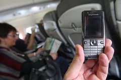 Eine Hand hlt ein ausgeschaltetes Handy in einem Flugzeug.