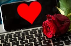 Eine Rose liegt auf einer Computertastatur. Im Hintergrund ist ein Smartphone zu sehen, auf dem ein Herz abgebildet ist.