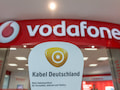 Das Logo des Kabelnetzbetreibers Kabel Deutschland vor dem Schriftzug des Mobilfunkanbieters Vodafone an einem Vodafone-Geschft.
